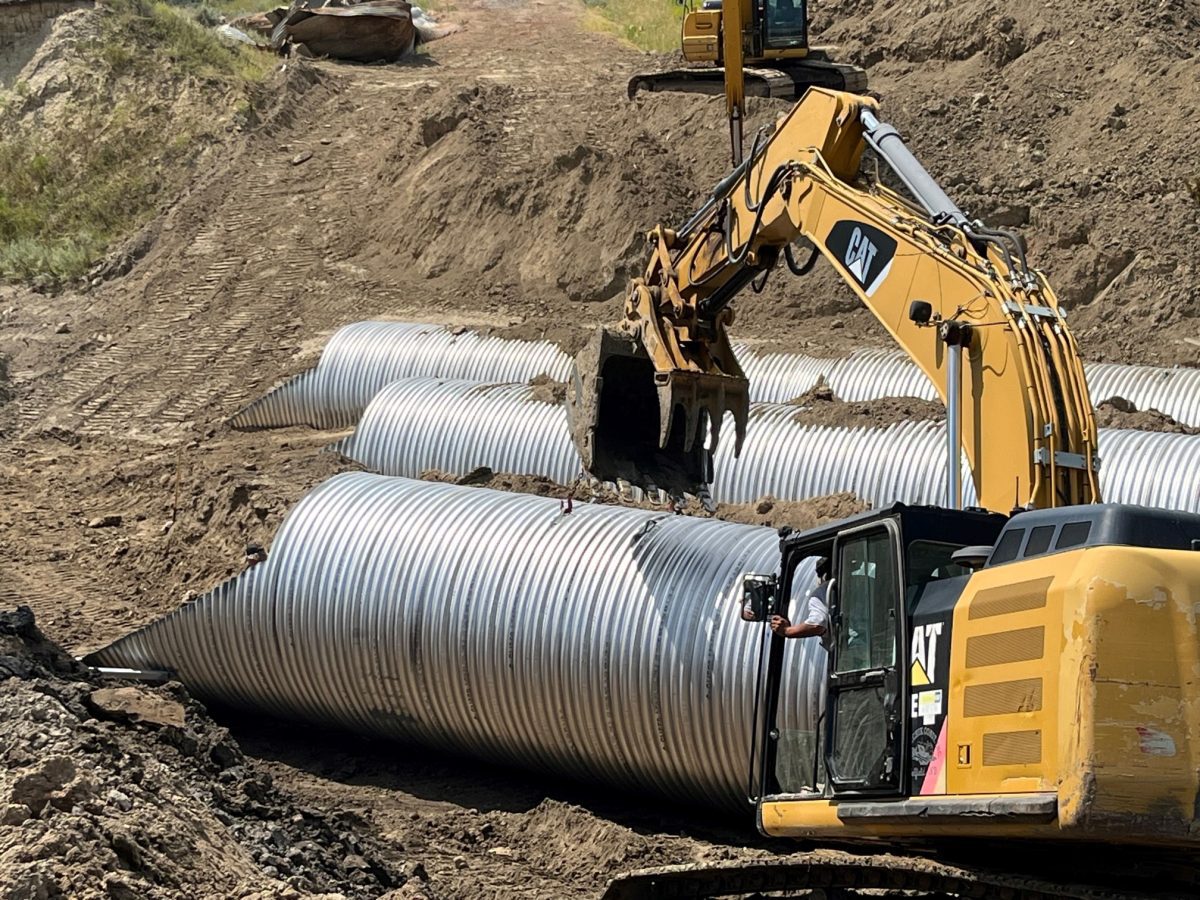Three large corrugated steel pipes next to a large piece of excavation equipment